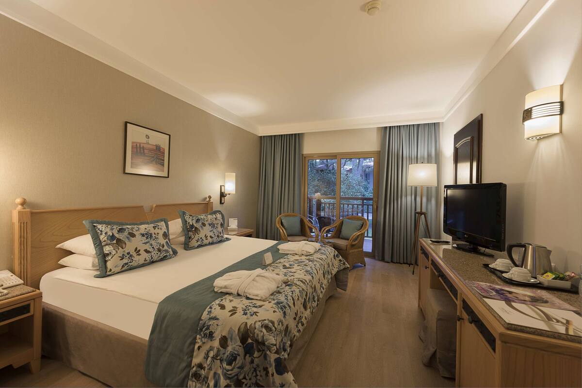 A hotel room with a large bed, a desk with a television, a chair, and a window with curtains.