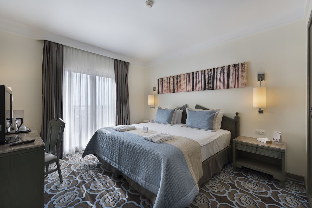 A hotel room with a large bed, a desk with a chair, a flat-screen TV, and a painting on the wall.