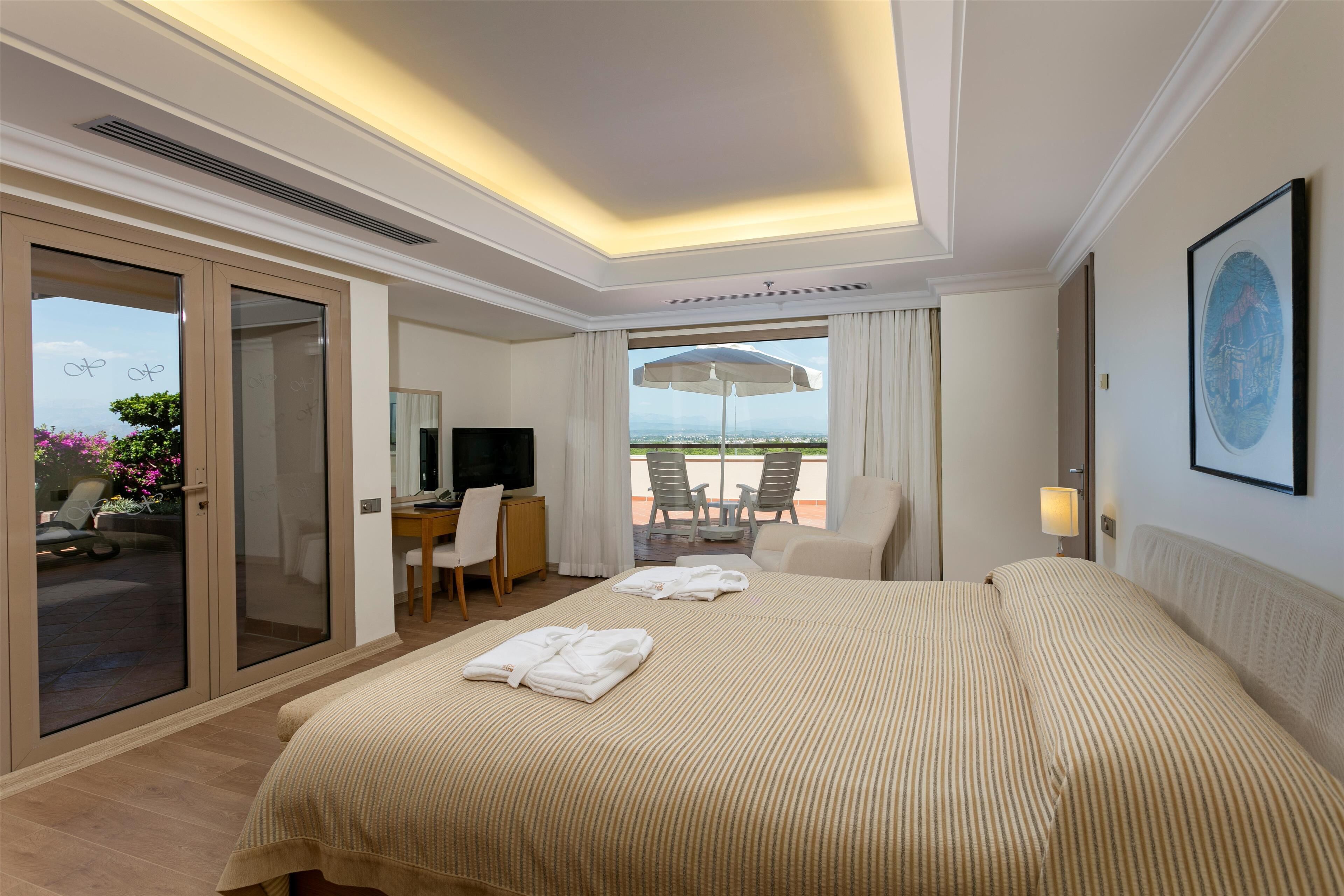 Een hotelkamer met een bed, een bureau, een televisie en een balkon met stoelen.