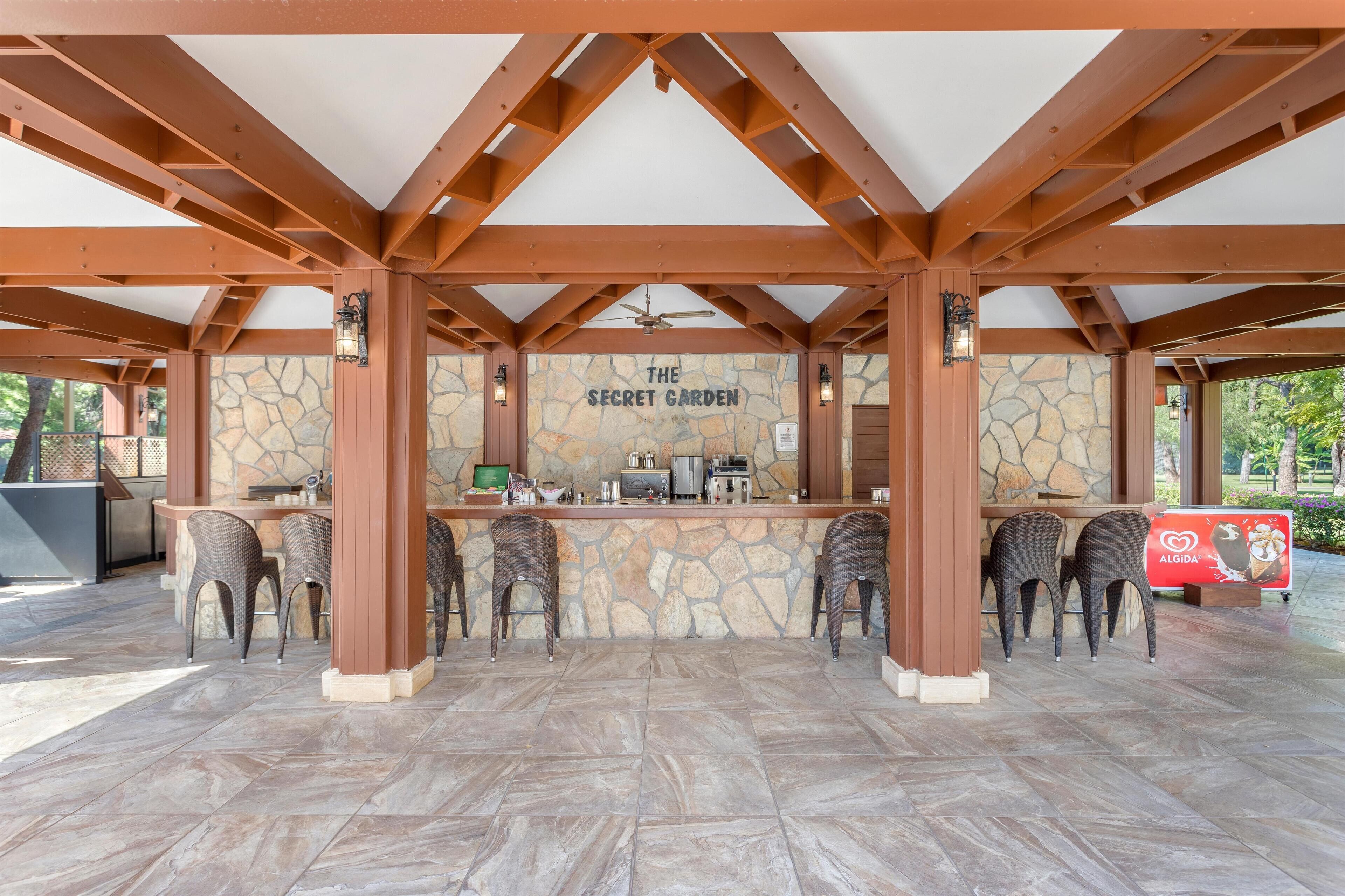 Un patio al aire libre con pared de piedra, vigas de madera y sillas de mimbre.