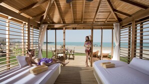 A wooden deck with two beds, a table, and chairs overlooking a beach. - Xanadu Resort Hotel - High Class (Serik)