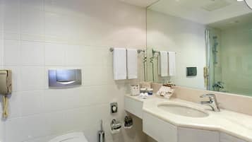 A modern bathroom with a large sink, mirror, and shower. There is a toilet, a bidet, and a toilet paper holder.