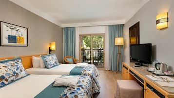 Habitación de hotel con dos camas, un escritorio con televisor y un balcón con mobiliario de exterior.