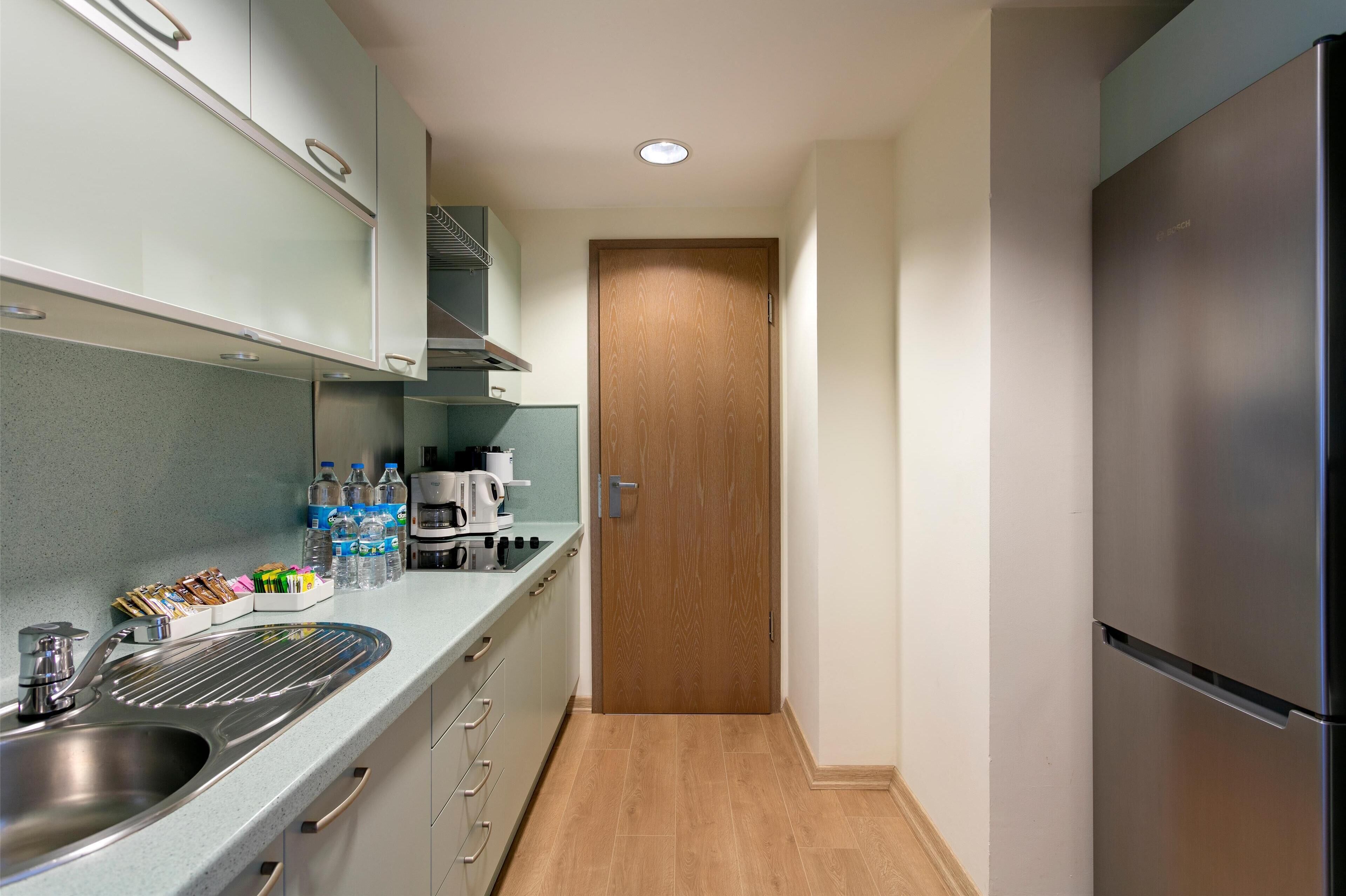 A modern kitchen with a stainless steel sink, a refrigerator, and a wooden door.