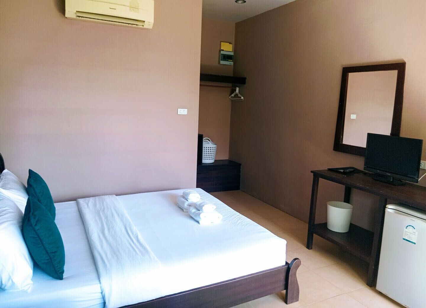 A hotel room with a bed, a desk with a television, a small refrigerator, and a mirror on the wall.