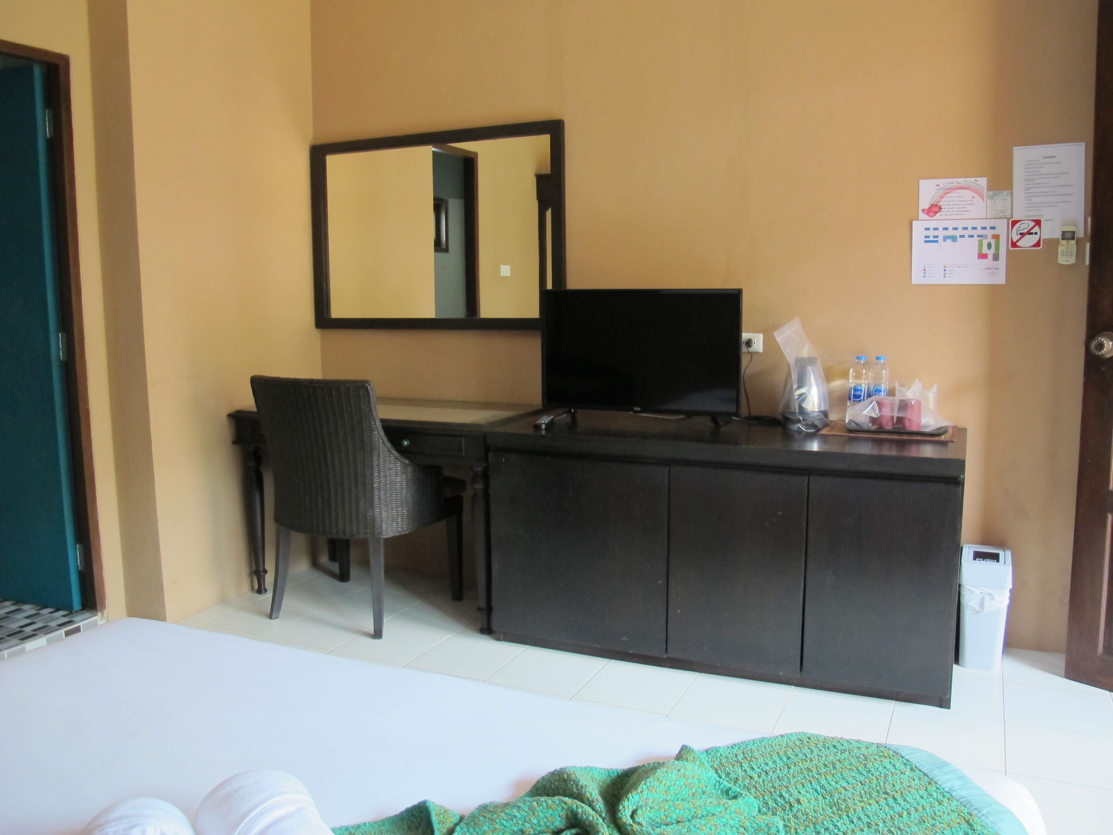 A hotel room with a bed, a desk with a computer, a chair, a mirror, and a small trash bin.