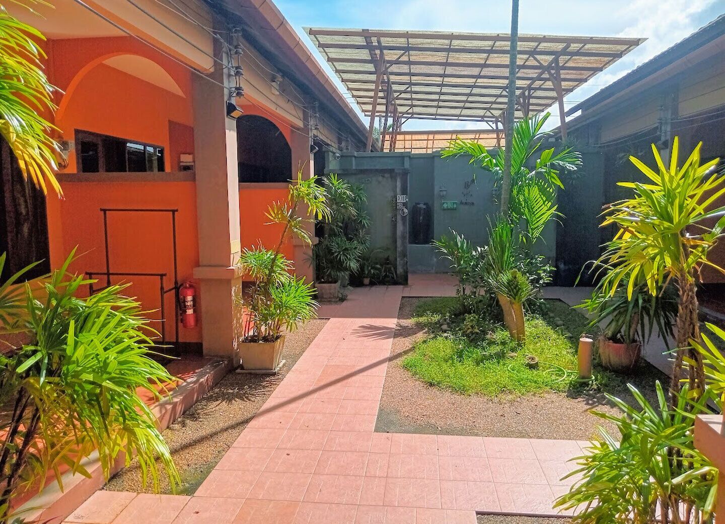 A courtyard with potted plants, a tiled walkway, and a covered area with a metal roof.