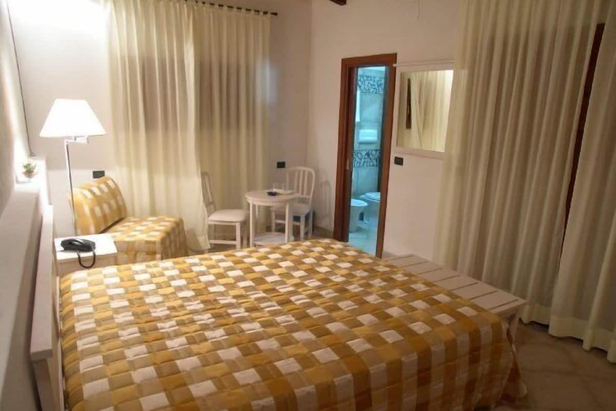 A hotel room with a checkered bedspread, a desk, a chair, a lamp, and a bathroom visible through a door.