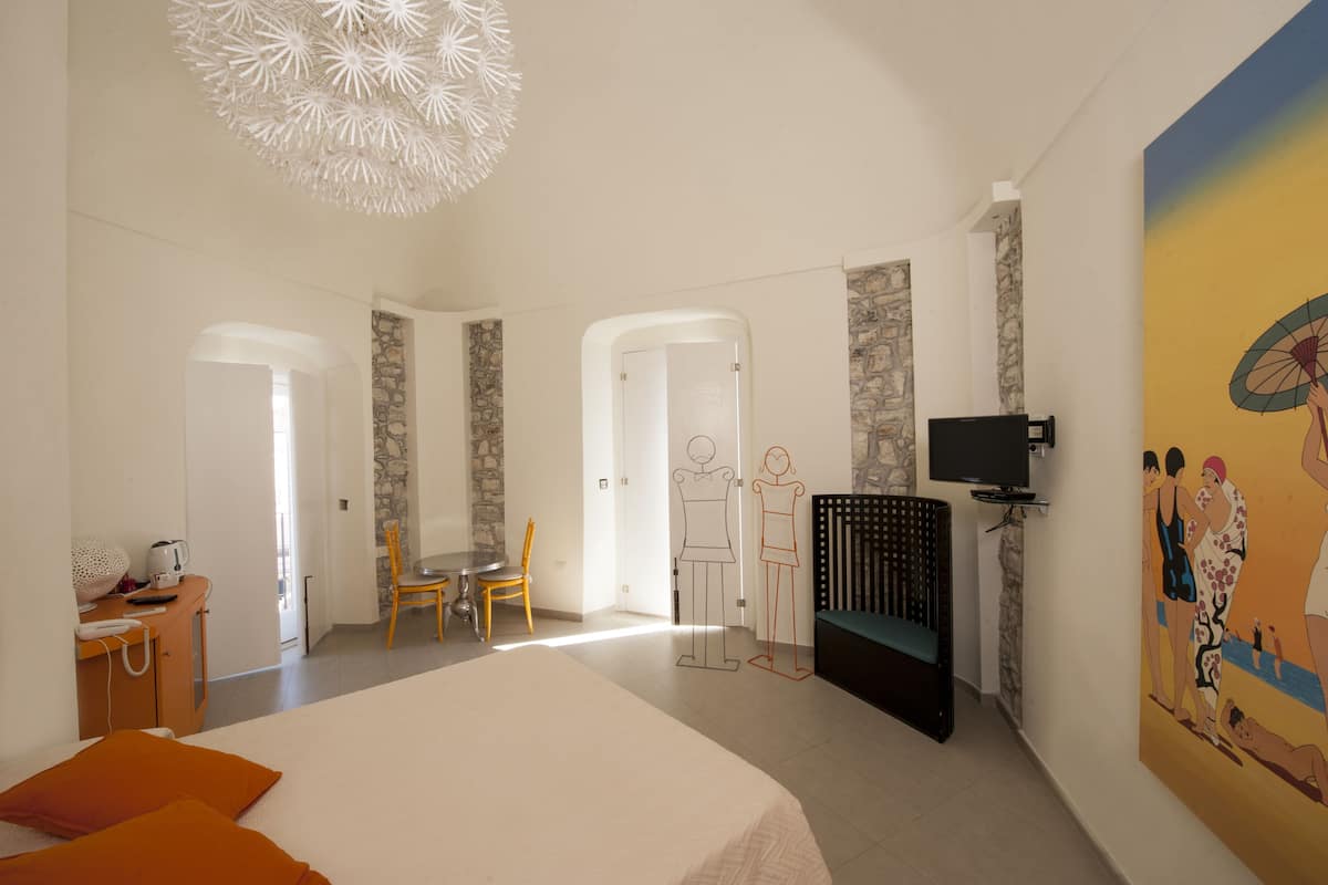 Una habitación de hotel con una cama grande, un escritorio con teléfono, una silla, un televisor y un cuadro en la pared.