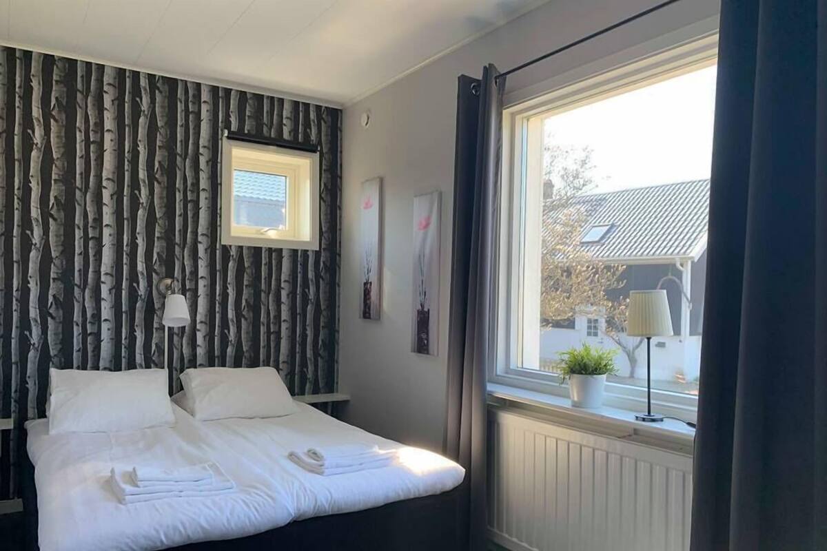 A neatly made bed with white linens, a bedside lamp, and a window with curtains.