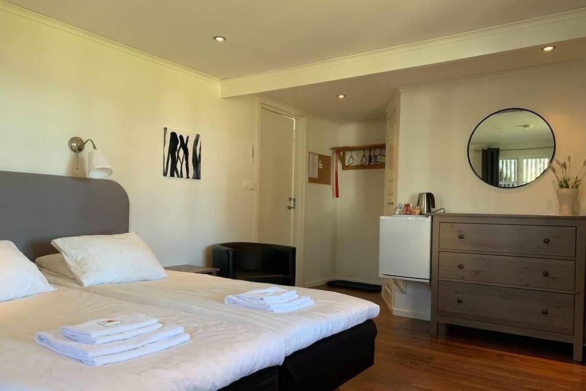 A modern bedroom with a large bed, a dresser, a mirror, and a small seating area.