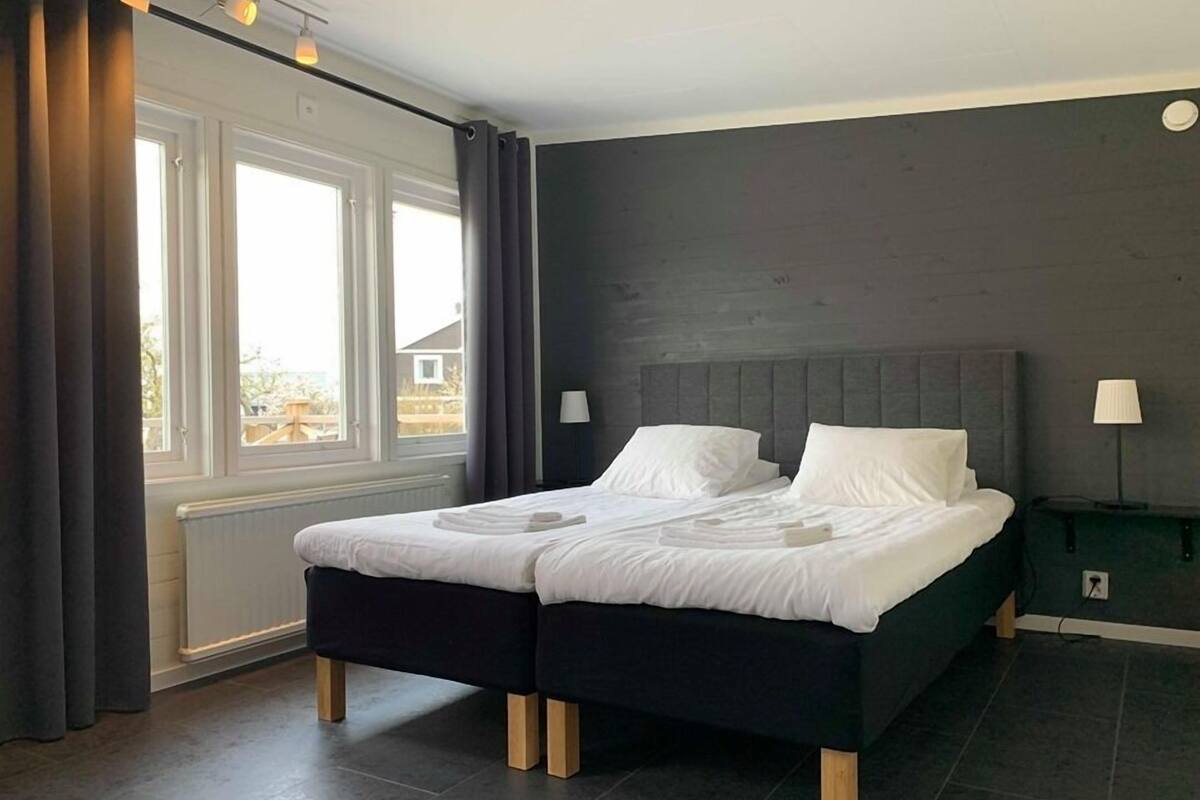 A modern bedroom with a double bed, dark walls, and a view through a window.