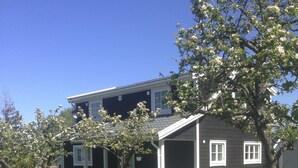 Ein zweigeschossiges Haus mit Veranda, umgeben von einem grünen Rasen und blühenden Bäumen.