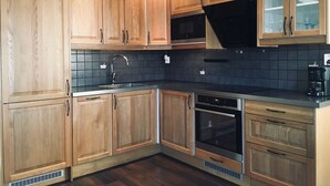 Eine moderne Küche mit Holdekor-Schränken, einer schwarzen Küchenrückwand aus Fliesen, Edelstahlgeräten und einem eingebauten Backofen.