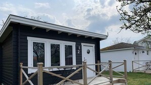 Eine kleine, zweistöckige Holzhütte mit einer Holzterrasse und einem Metallzaun.
