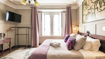 A hotel room with a bed, a television, a radiator, and a window with curtains.
