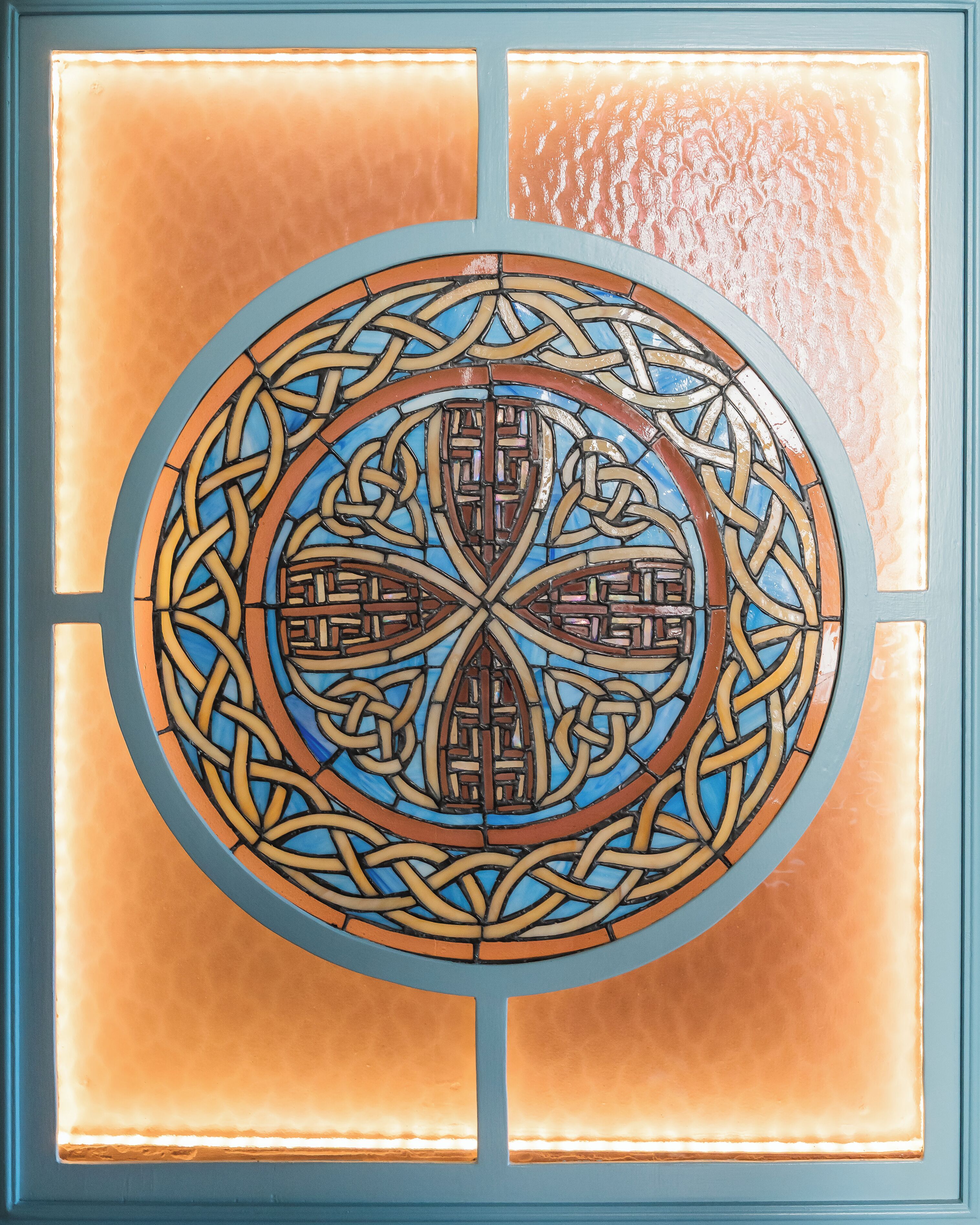 A stained glass window with a circular design, featuring intricate patterns and a blue border.