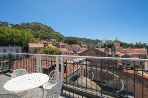 A balcony with a table and chairs, overlooking a town with historic buildings and a hill in the background. - Chalet Saudade (Sintra)