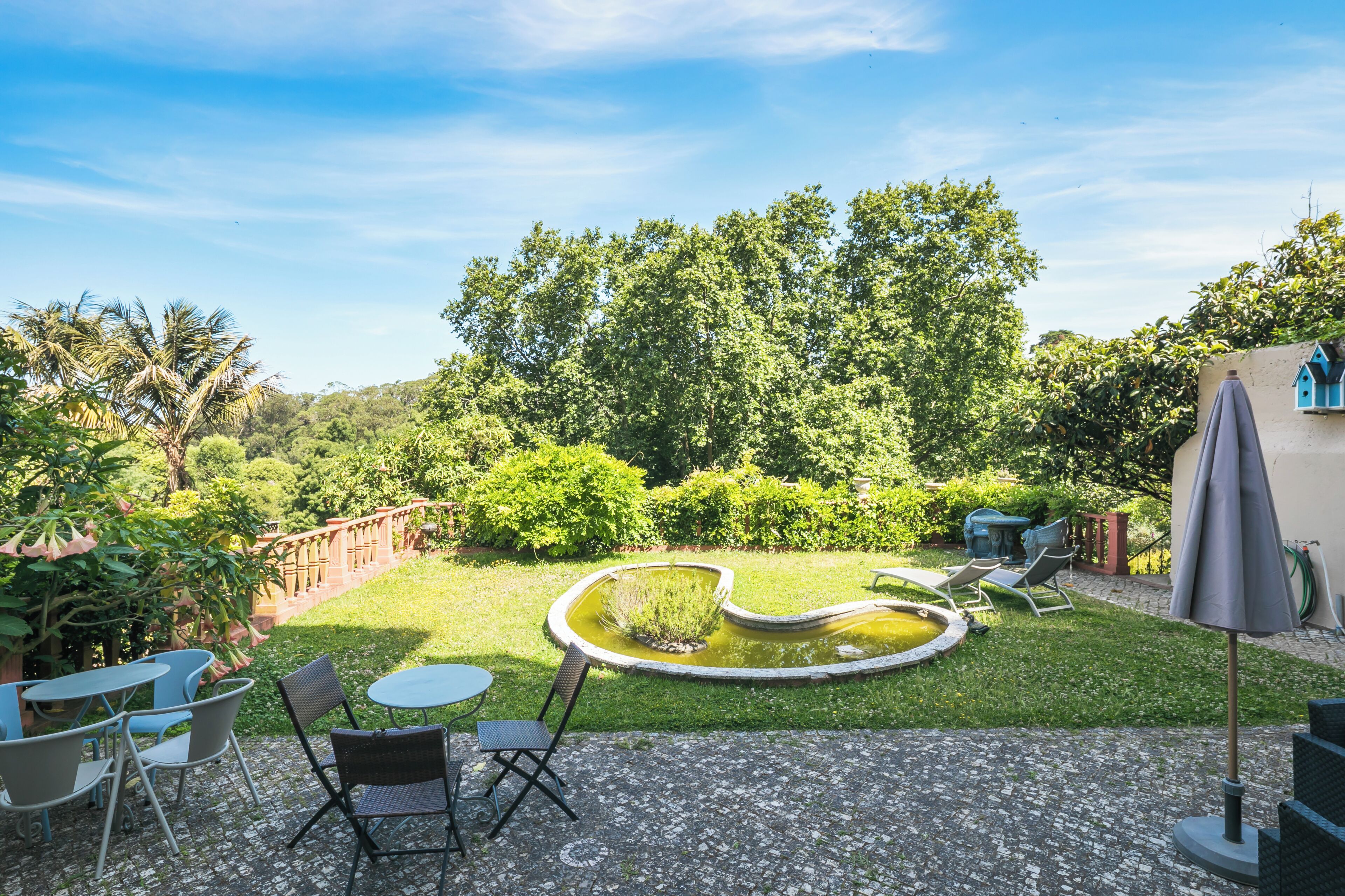A garden with a circular pond, seating area with chairs and tables, and a gazebo.