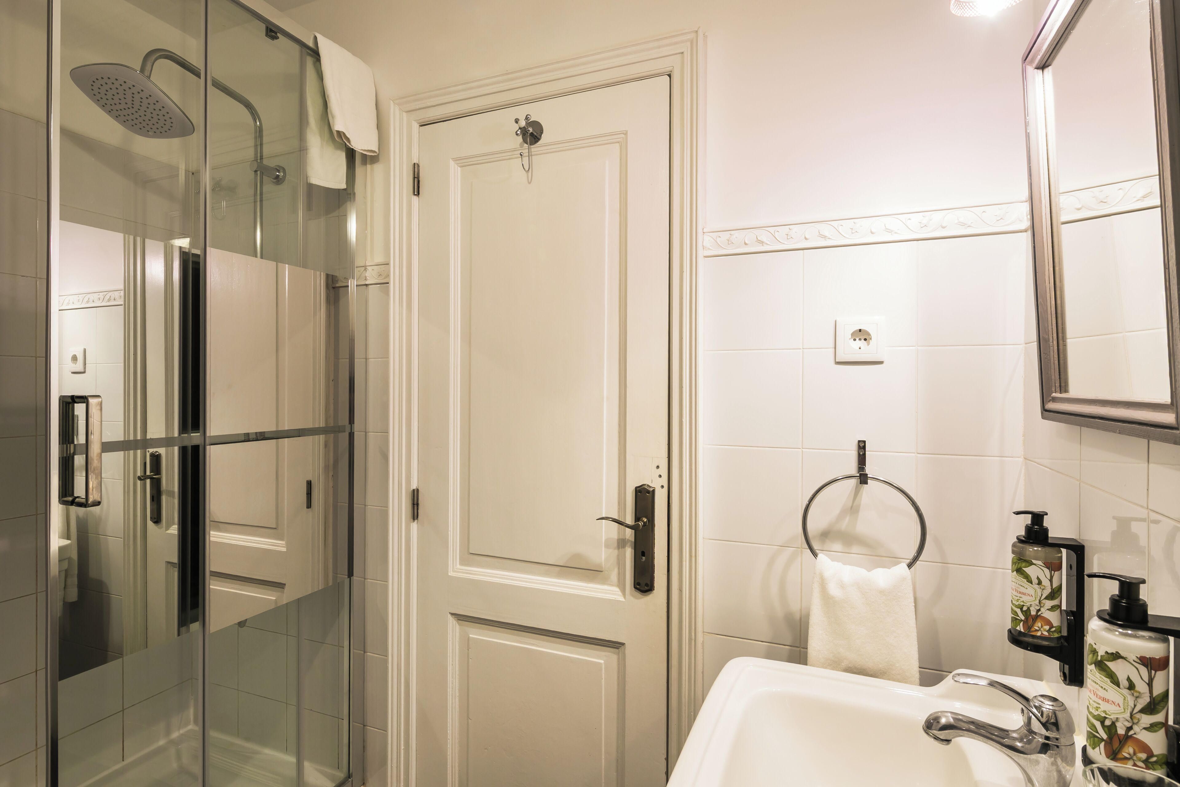 A bathroom with a glass-enclosed shower, a white sink, and a mirror.