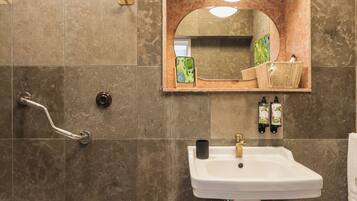 A bathroom with a white pedestal sink, a mirror with a wooden frame, and a handrail.