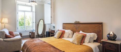 A bedroom with a large bed, a bedside table, a lamp, a dresser, and a mirror.