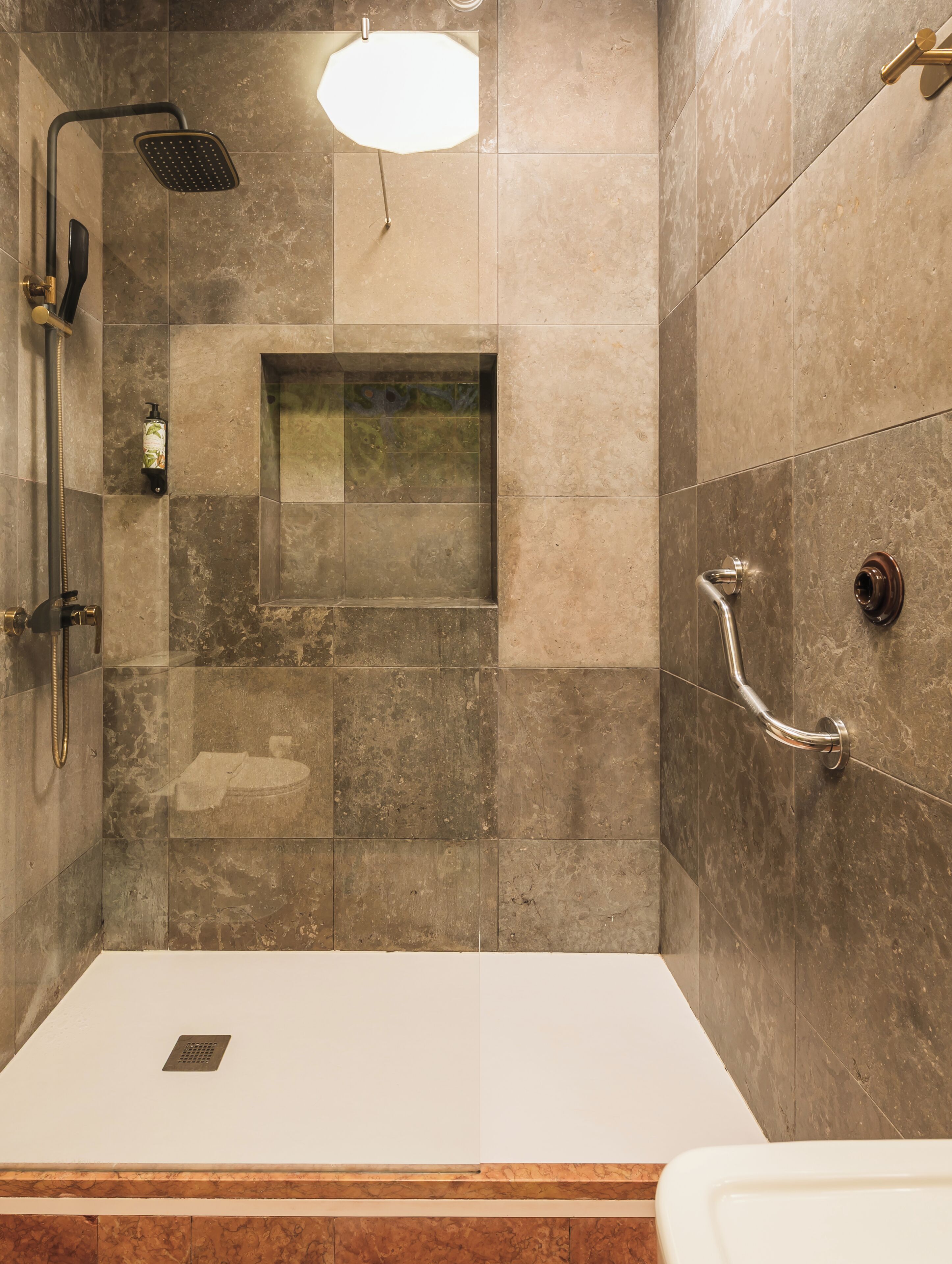 A modern bathroom with a shower, a handrail, and a toilet.