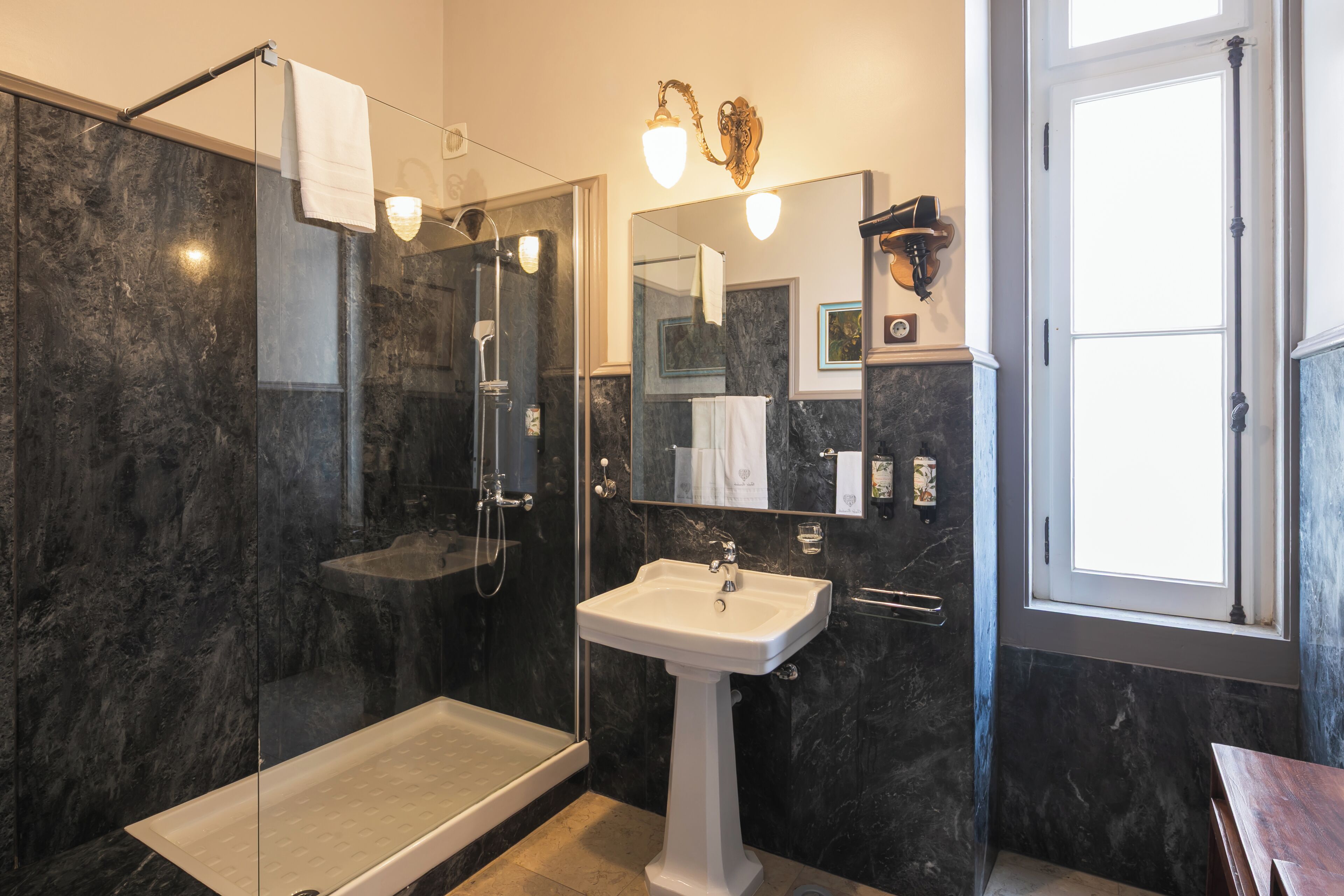 Un baño moderno con ducha de vidrio, lavamanos pedestal y un espejo grande.