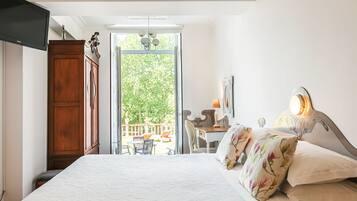 Une chambre dotée d’un grand lit, d’un bureau et d’une chaise, d’une armoire en bois, et offrant une vue sur un balcon aménagé avec du mobilier d’extérieur.