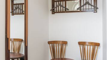 A hallway with a wooden floor, a mirror, two wooden chairs, and a wall-mounted coat rack.