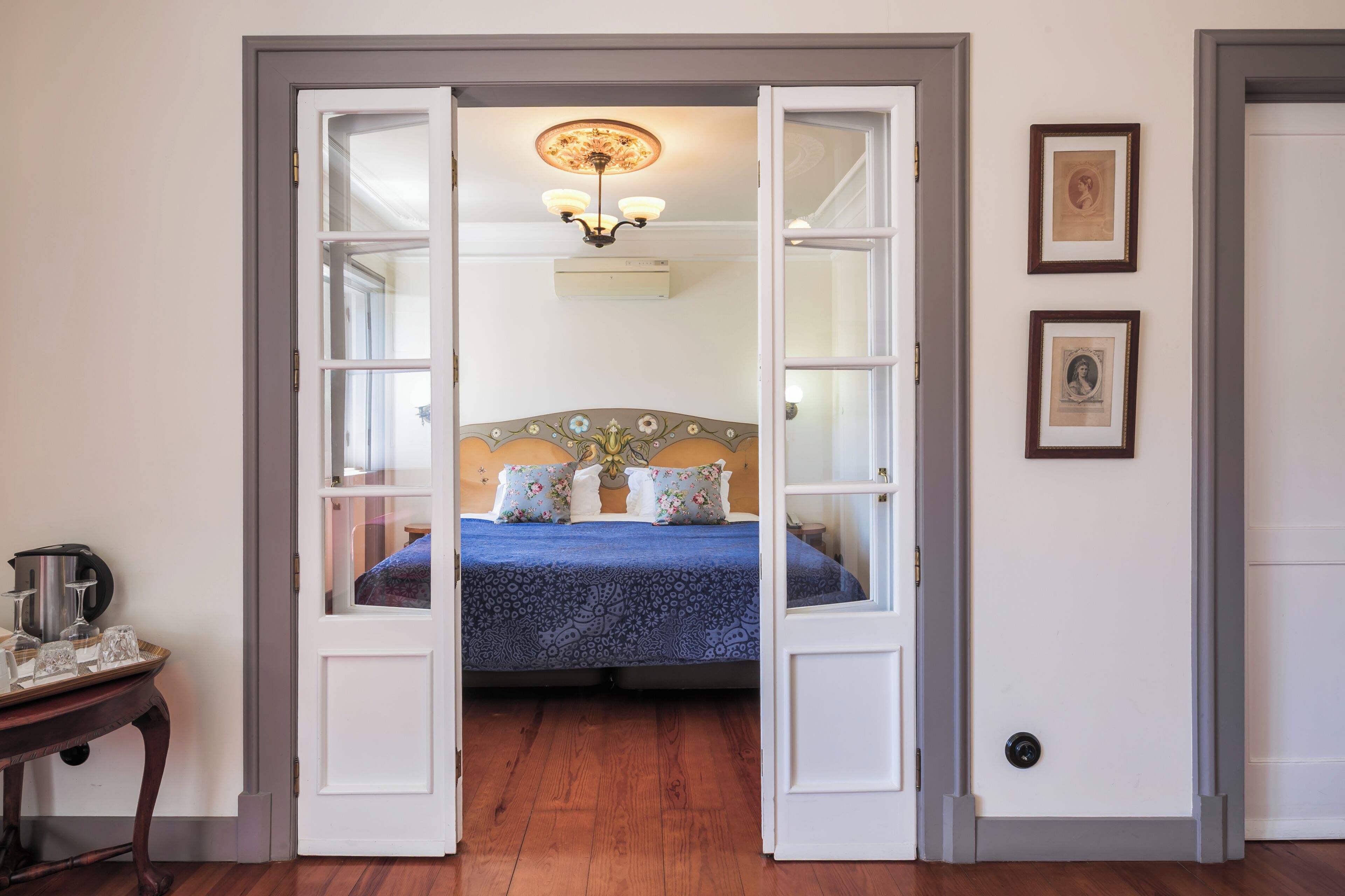 A bedroom with a bed, a chandelier, and a door leading to another room.