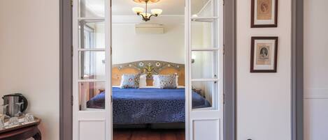 A bedroom with a bed, a chandelier, and a door leading to another room.