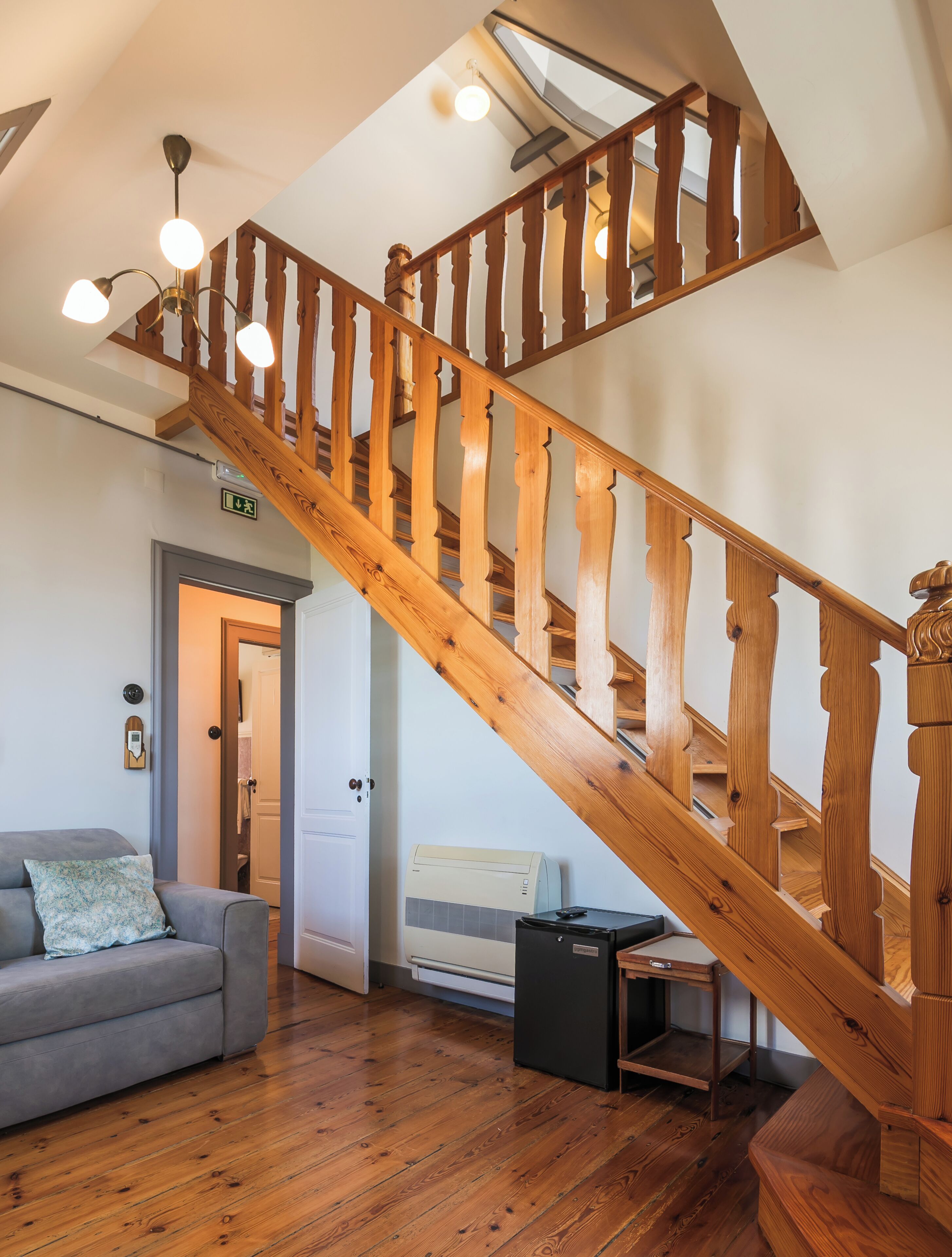 A wooden staircase with a handrail, a grey sofa with a patterned pillow, and a ceiling light fixture.