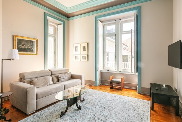 A living room with a sofa, a glass coffee table, a lamp, a TV, and a window with a view. - Chalet Saudade (Sintra)