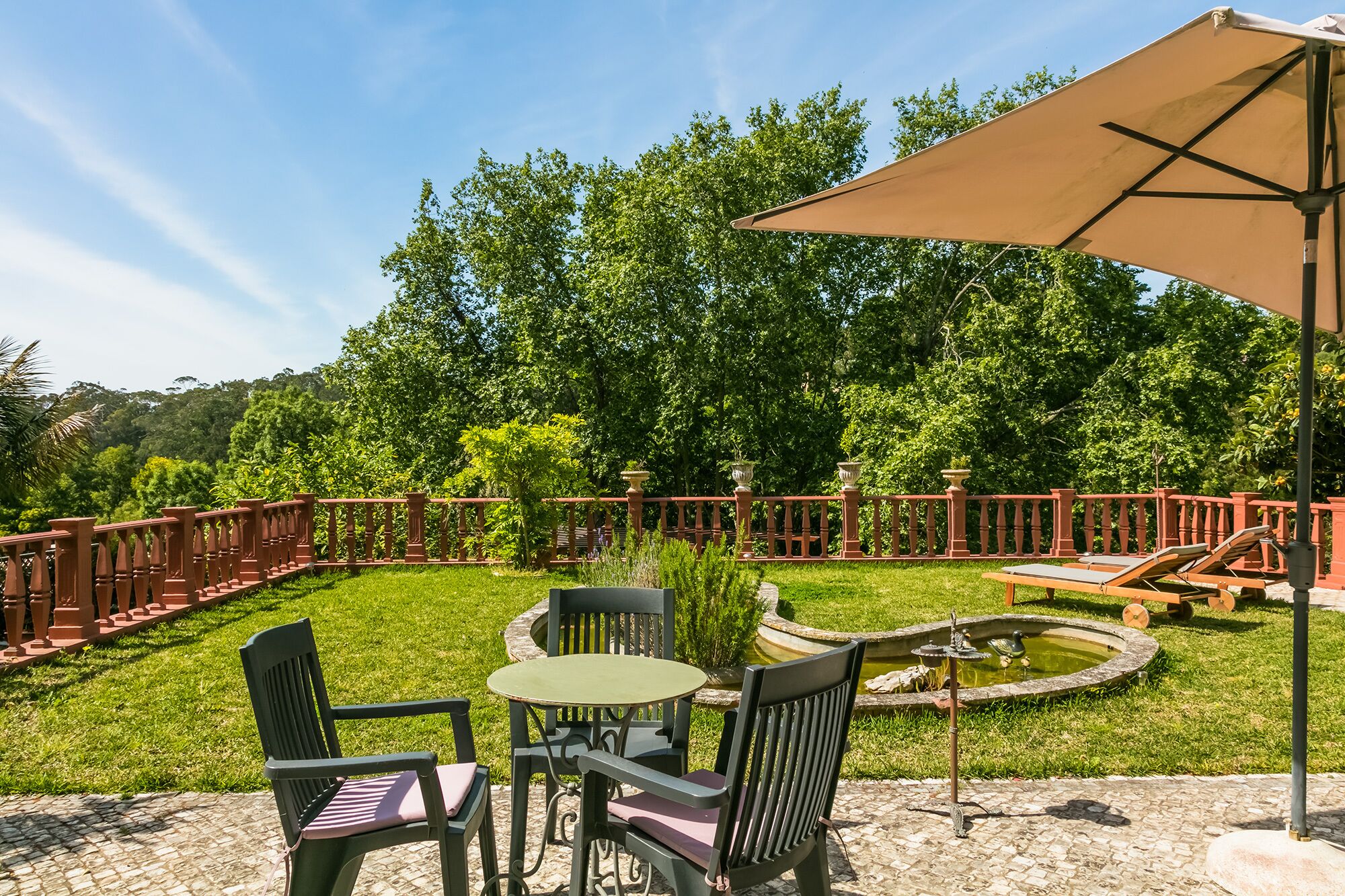 Une terrasse extérieure avec une table ronde et des chaises, une petite fontaine et une clôture rouge.
