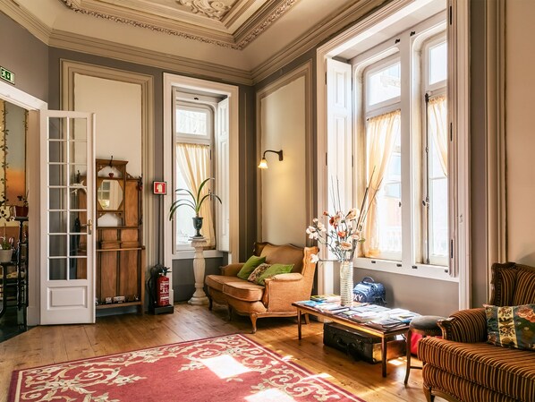 A spacious living room with a wooden floor, a red patterned rug, a sofa, a coffee table, and a window with curtains. - Chalet Saudade (Sintra)