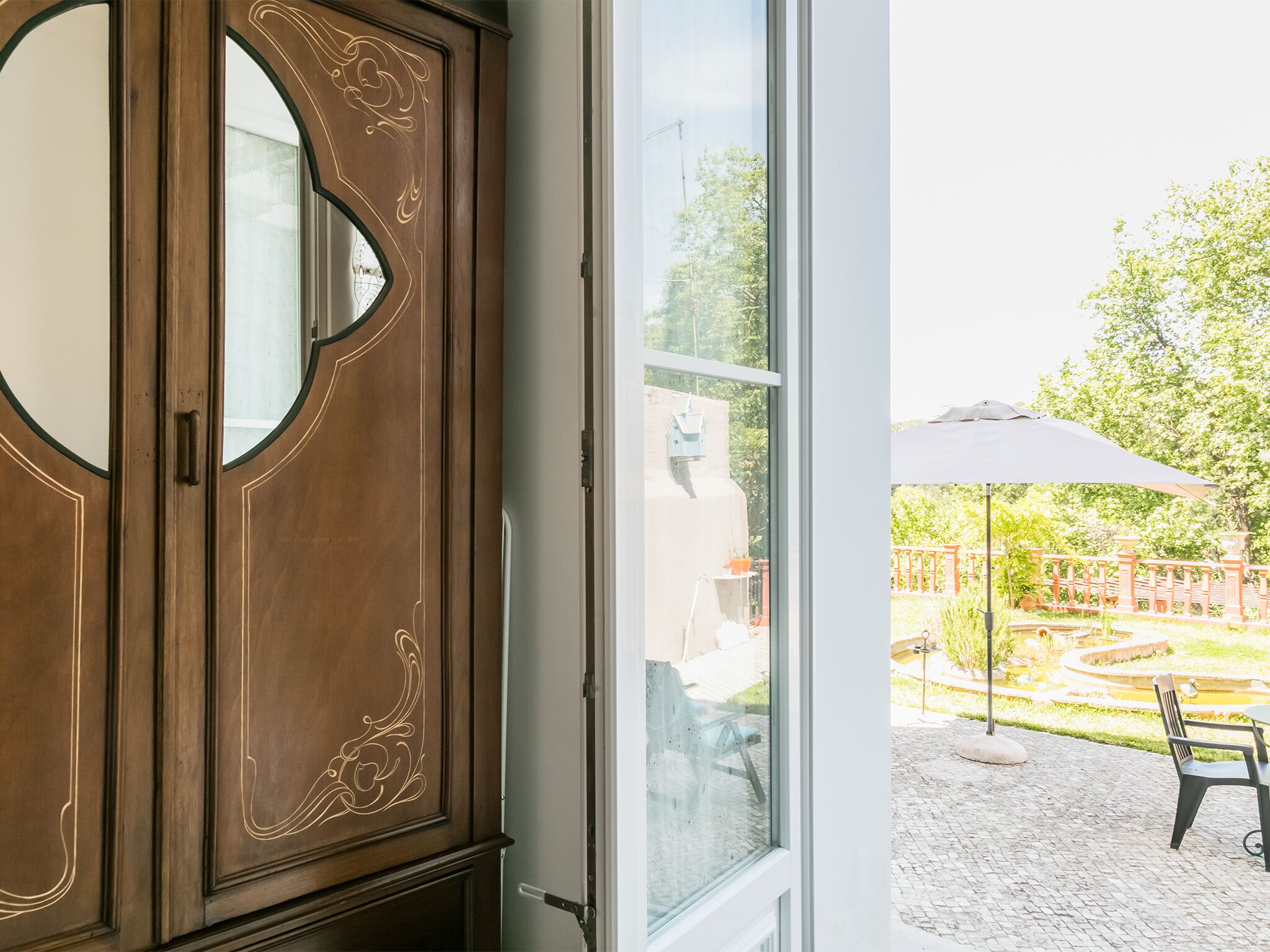 A wooden cabinet with a circular mirror and a glass door leading to an outdoor patio area with a table, chairs, and an umbrella.