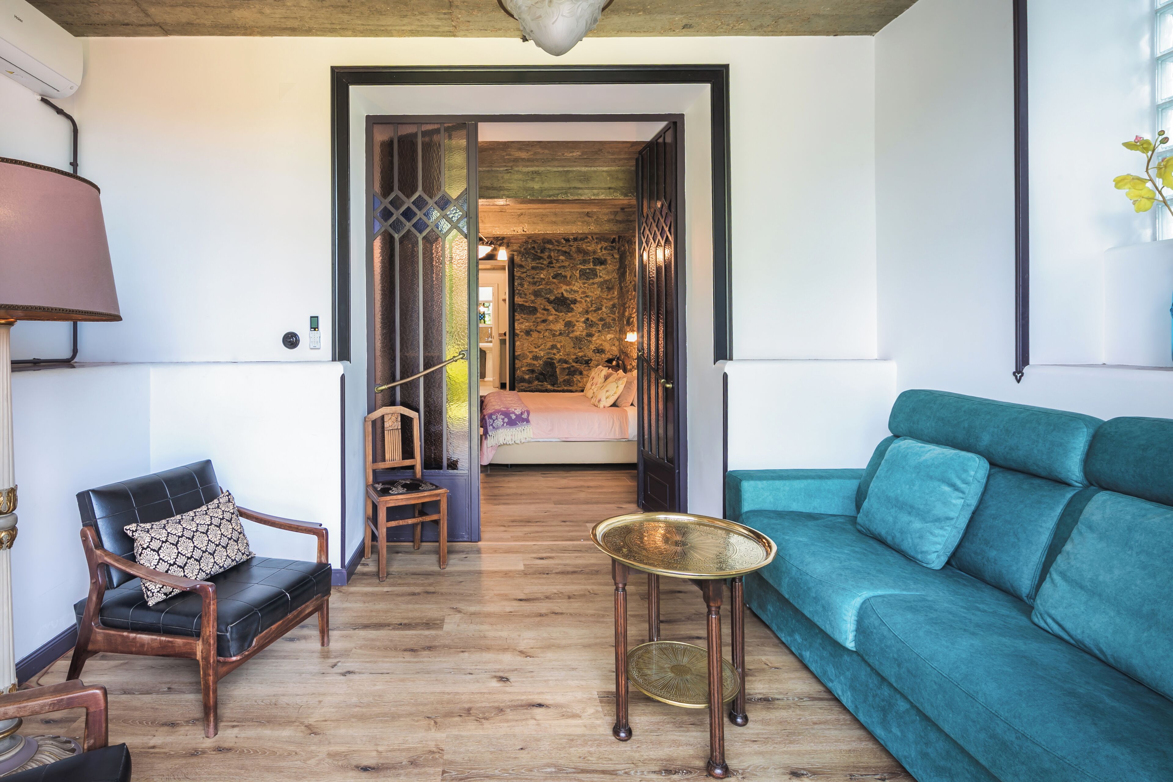 Un salon moderne avec un canapé de couleur turquoise, un fauteuil en cuir noir, une petite table ronde et un plancher en bois.
