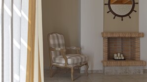 A room with a fireplace, a plaid armchair, and a round mirror on the wall. - Dialiskari Villas (Trifylia)