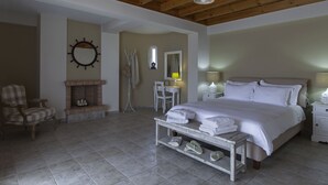 A bedroom with a bed, a chair, a small table with towels, a mirror, and a fireplace. - Dialiskari Villas (Trifylia)