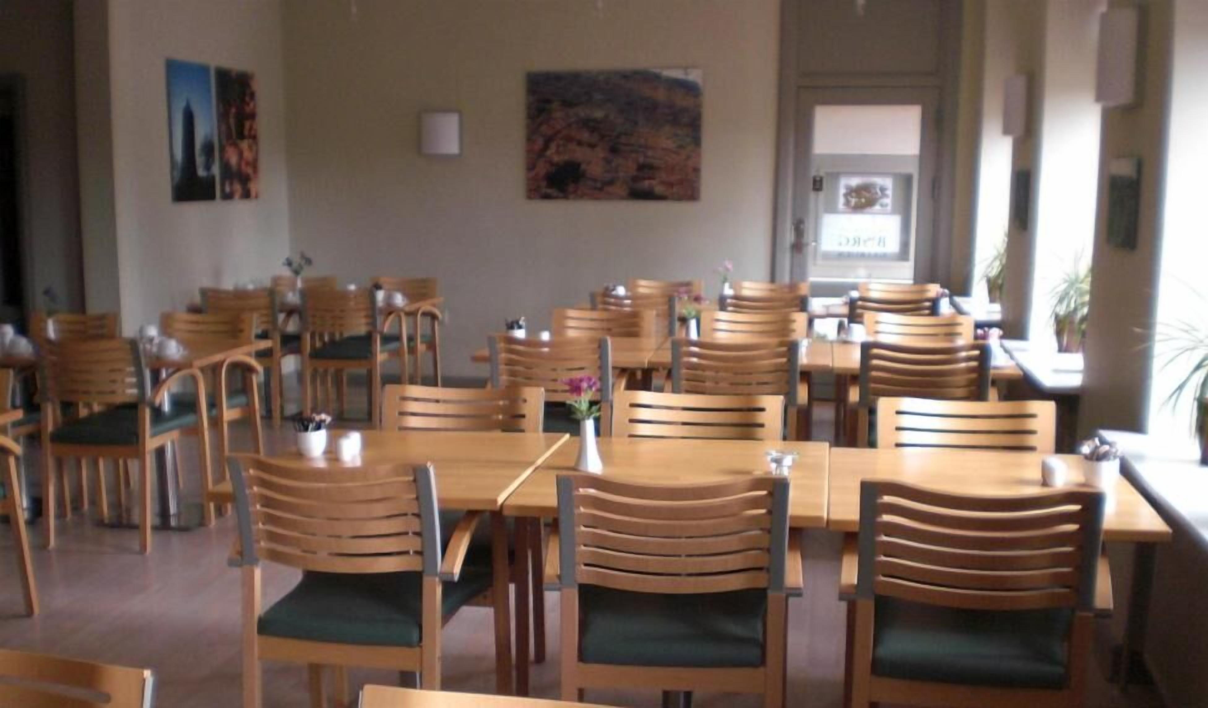 Un comedor con mesas y sillas de madera, un cuadro en la pared y una puerta con un letrero.