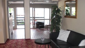 A hotel lobby with a red patterned carpet, a black leather sofa, a small round table, and a large mirror on the wall. - Hotel Kong Valdemar (Vordingborg)