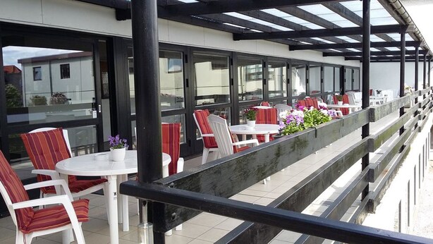An outdoor seating area with white tables and striped chairs, a wooden railing, and potted plants. - Hotel Kong Valdemar (Vordingborg)