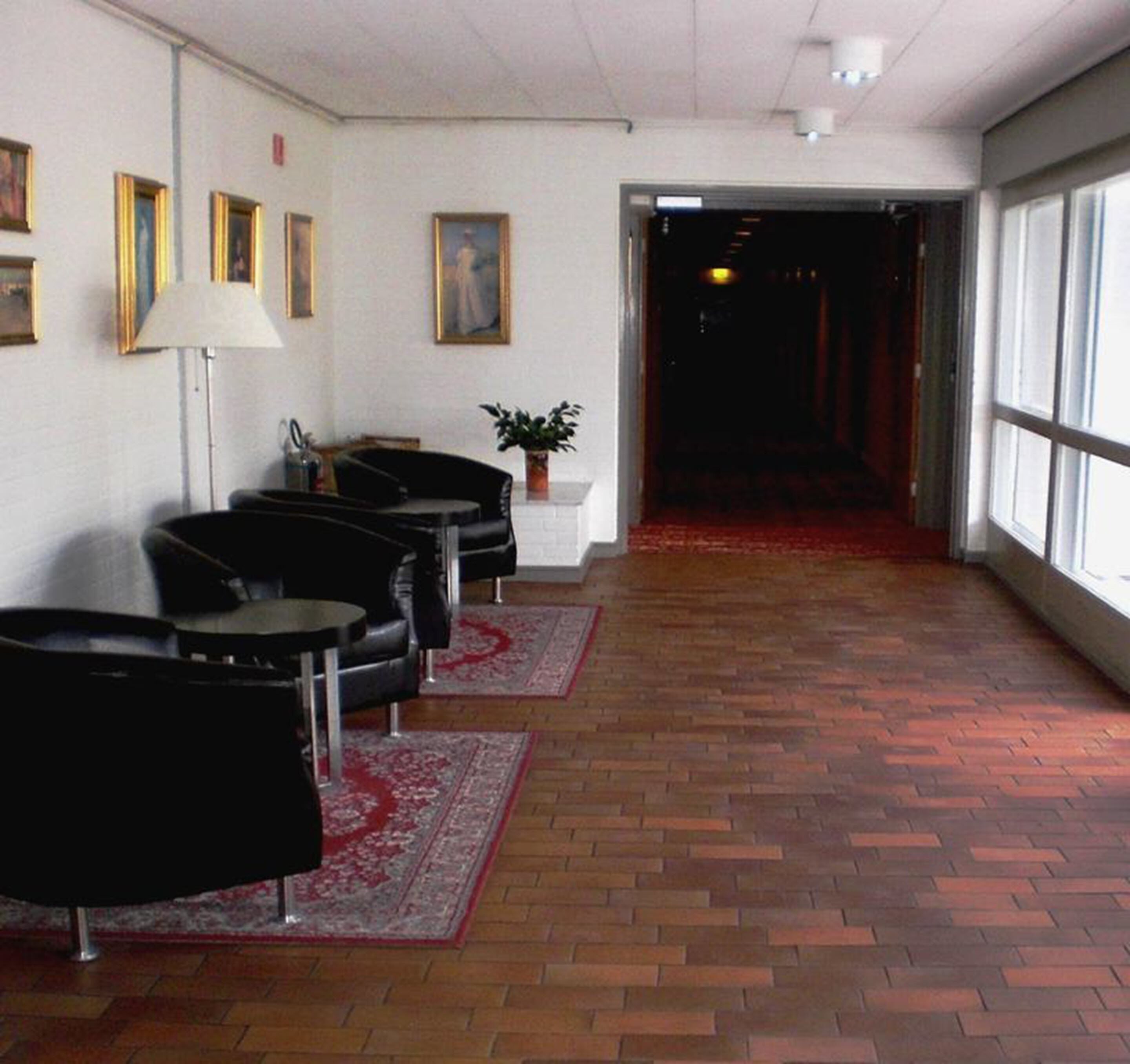 A hallway with black leather chairs, a white reception desk, and a potted plant.