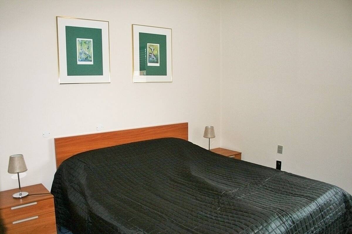 A neatly made bed with a dark quilt, two framed pictures on the wall, and bedside lamps on wooden nightstands.