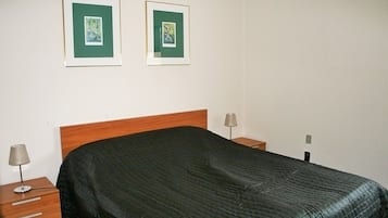 Een net opgemaakt bed met een donge deken, twee ingelijste foto’s aan de muur en bedlampen op houten nachtkastjes.