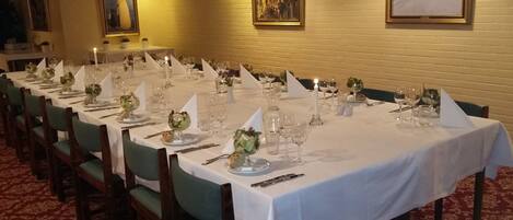 A long dining table set for a formal event with white tablecloths, green chairs, and floral centerpieces.