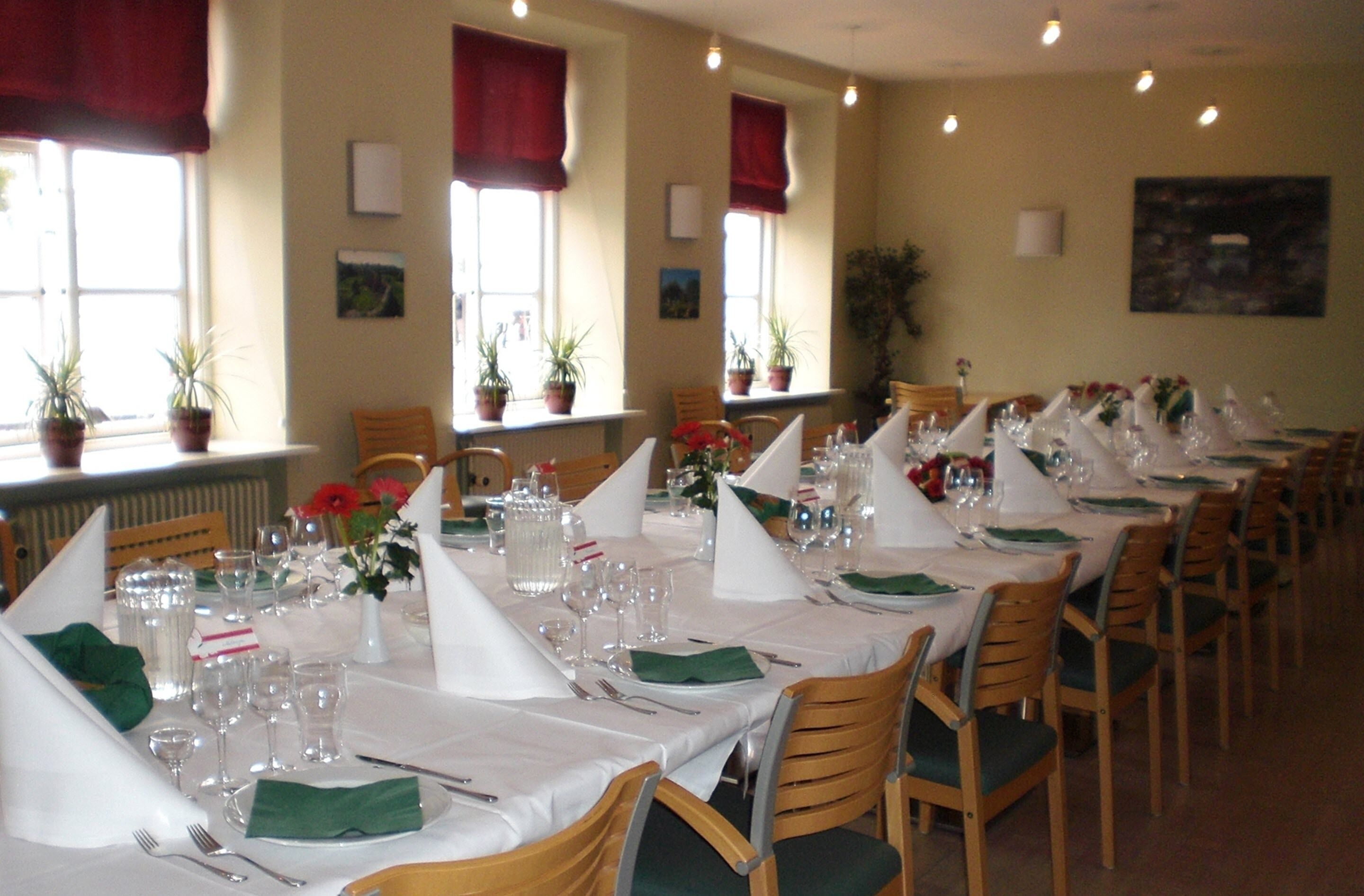 A dining area with multiple tables set for a meal, each with white tablecloths, green napkins, and silverware.