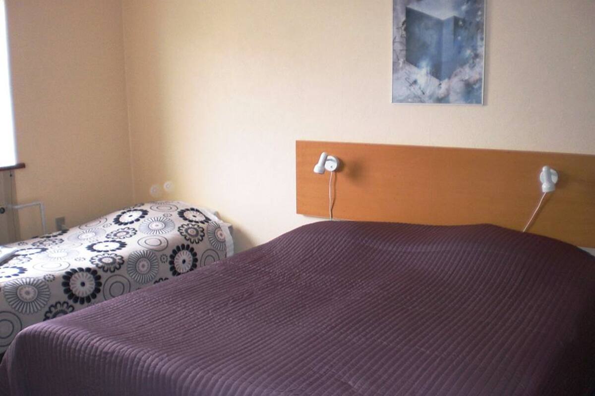 A room with two beds, one with a patterned bedspread and the other with a solid color bedspread.