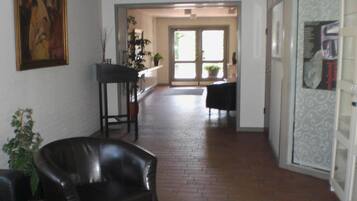 A spacious hallway with a brick floor, a black leather chair, a small table, and a door leading to another room.